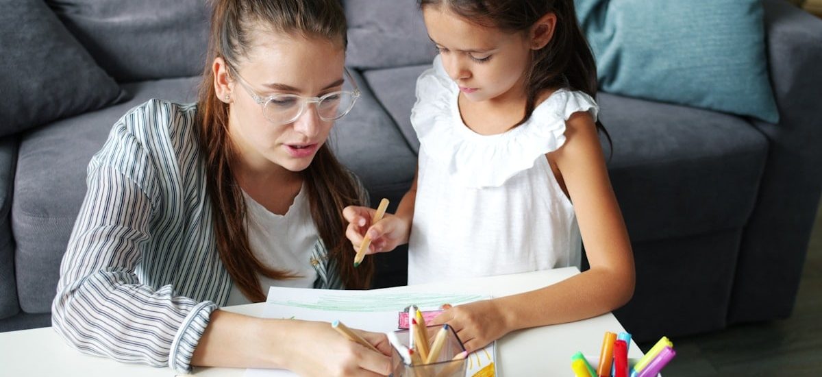 Happy family daughter and mother drawing picture at table in apartment, joyful kid is smiling enjoying hobby and mother's help. People and lifestyle concept.
