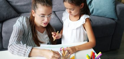 Happy family daughter and mother drawing picture at table in apartment, joyful kid is smiling enjoying hobby and mother's help. People and lifestyle concept.